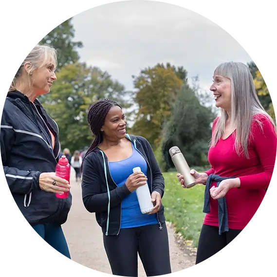 Three middle too late aged friends in a park with water bottles chatting and smiling